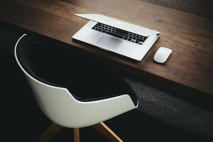 weißer Schalenstuhl vor zugeklapptem Laptop auf dunklem Holztisch