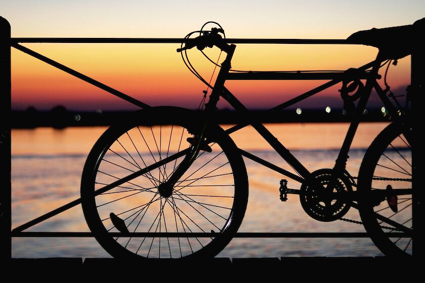 Fahrrad auf Brücke im Abendlicht, im Hintergrund Wasser